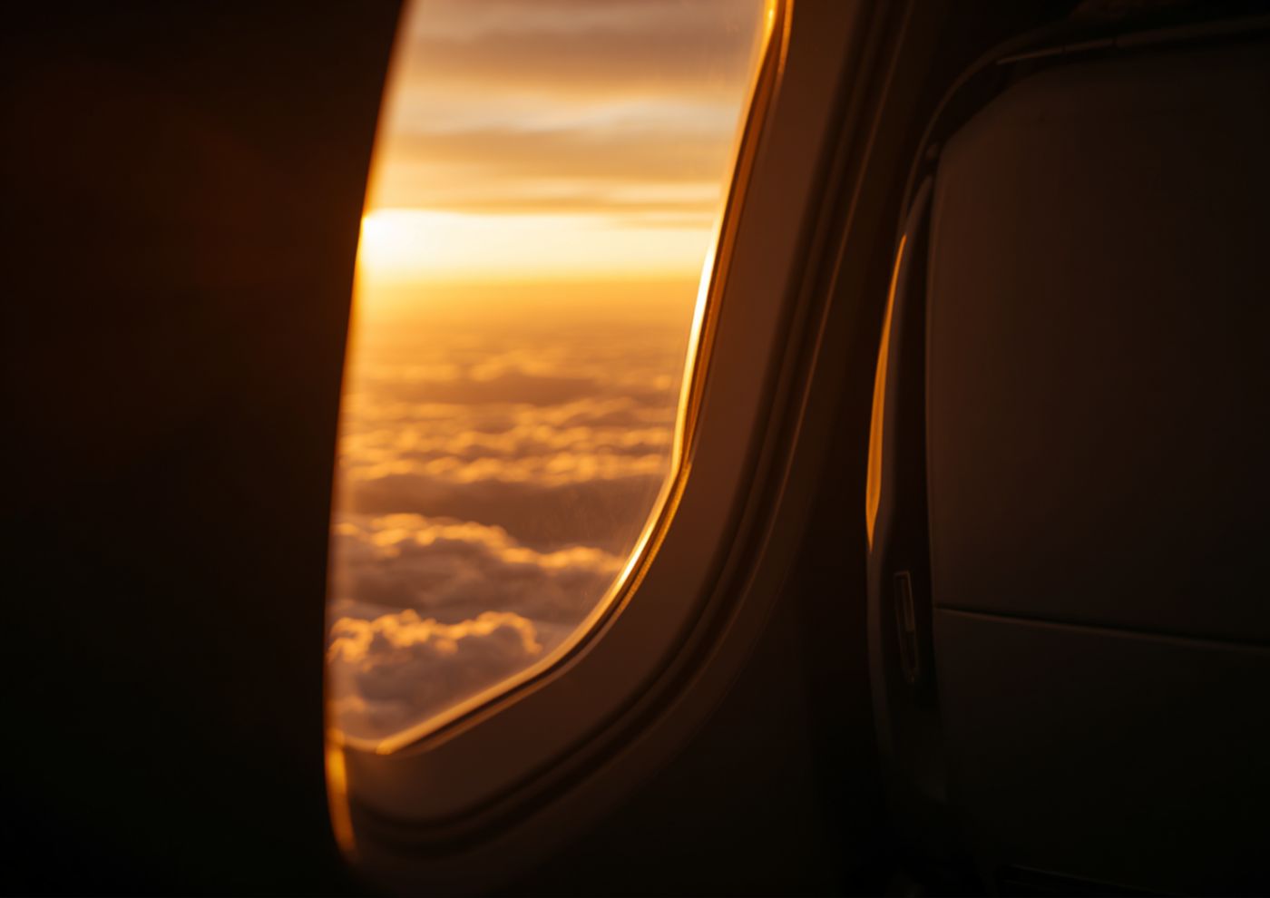 An airplane window view of clouds lit by a golden sunset.